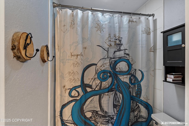 bathroom view of a textured wall, toilet, and curtained shower