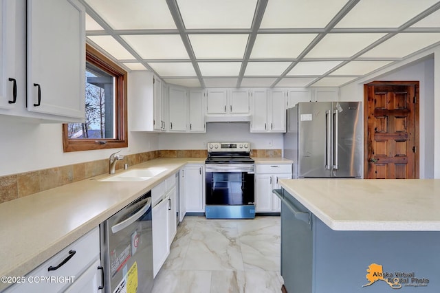 kitchen with appliances with stainless steel finishes, a sink, light marble finish floors, under cabinet range hood, and light countertops