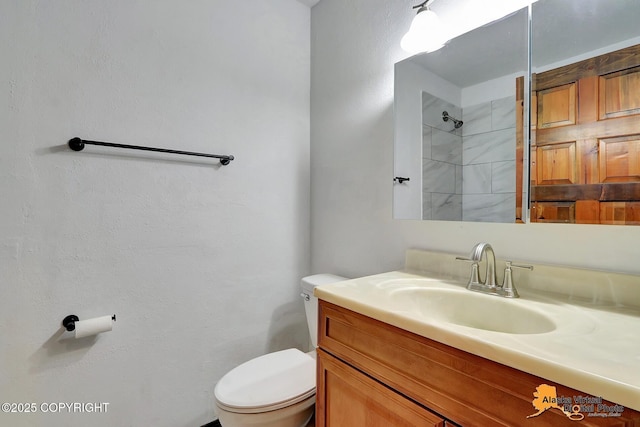 full bathroom with toilet, a tile shower, and vanity