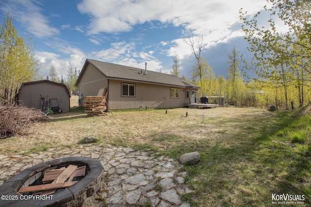rear view of house with a storage unit, an outdoor structure, a fire pit, and a yard