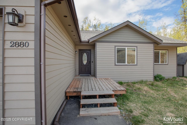 property entrance with a shingled roof and a lawn