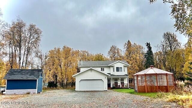 traditional-style house featuring an attached garage, gravel driveway, and view of wooded area