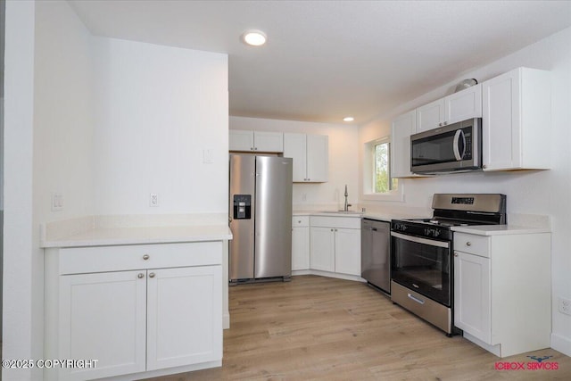 kitchen with stainless steel appliances, a sink, white cabinetry, light wood-style flooring, and recessed lighting