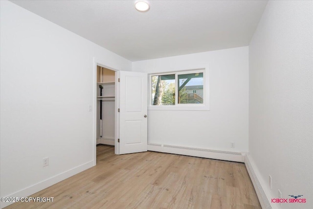 unfurnished bedroom with baseboards, light wood finished floors, a baseboard radiator, and a spacious closet