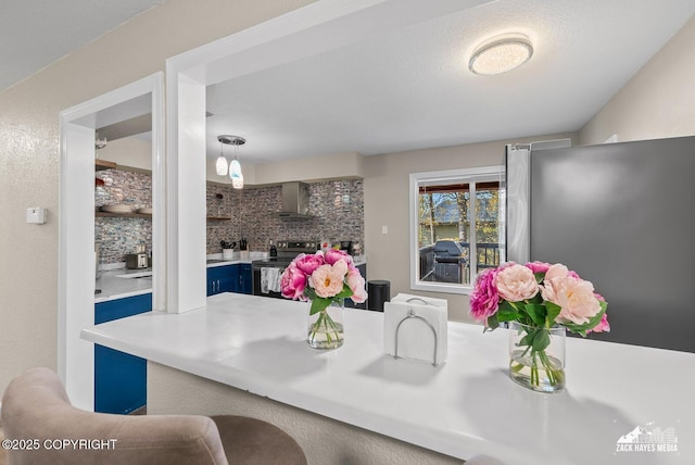 1507 W 47th Ave, Anchorage, AK 99503 - kitchen featuring electric range, wall chimney range hood, blue cabinets, freestanding refrigerator, and decorative backsplash