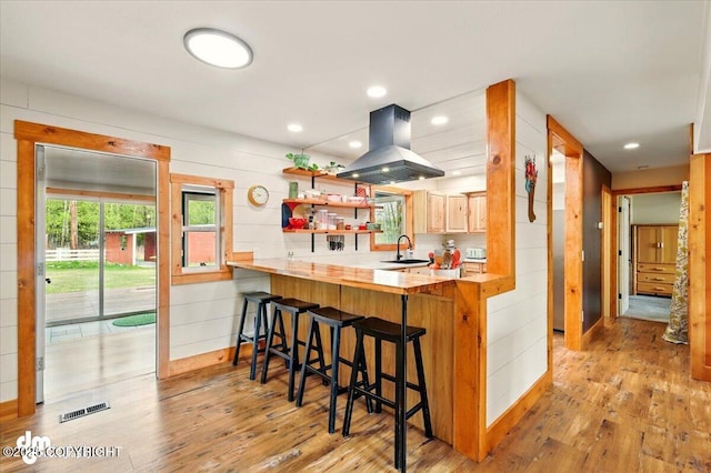 kitchen featuring island range hood, light wood finished floors, a breakfast bar area, wood counters, and open shelves