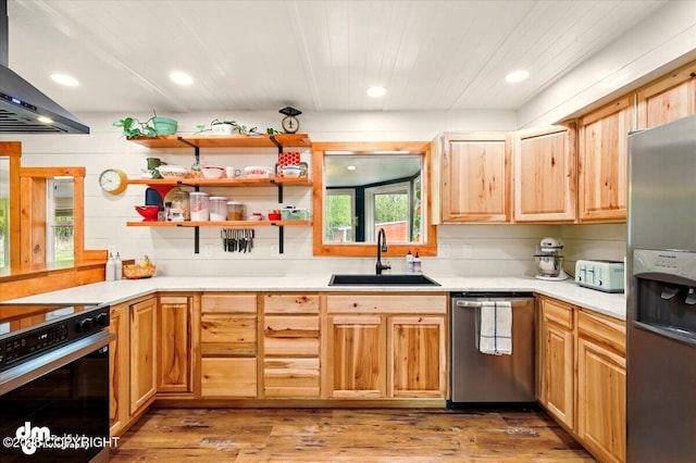 kitchen featuring a sink, stainless steel appliances, wall chimney exhaust hood, light wood-style floors, and wooden ceiling