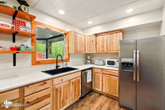 kitchen with stainless steel appliances, a sink, wood finished floors, recessed lighting, and light stone countertops