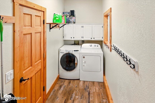 laundry area with cabinet space, washer and dryer, wood finished floors, and a textured wall