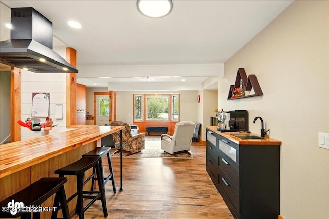 bar with island exhaust hood, a sink, light wood finished floors, and recessed lighting