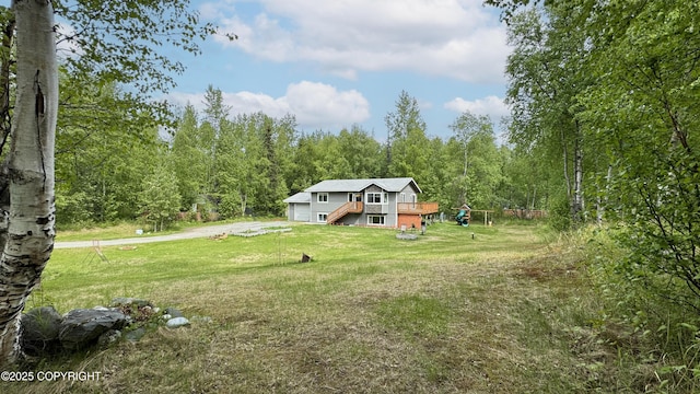 2435 N Ravens Flight Dr, Wasilla, AK 99654 - view of grassy yard with a wooden deck, a garage, a view of trees, driveway, and stairway