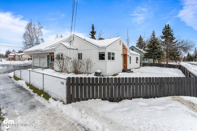 view of snow covered exterior featuring a fenced front yard and a garage