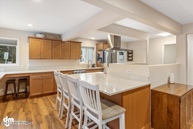 kitchen with island exhaust hood, a kitchen bar, light wood-type flooring, a sink, and light stone countertops