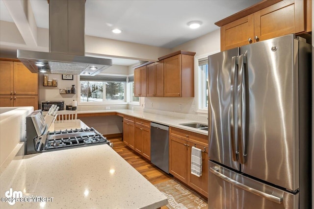 kitchen featuring stainless steel appliances, island range hood, light wood-style flooring, light stone counters, and a sink