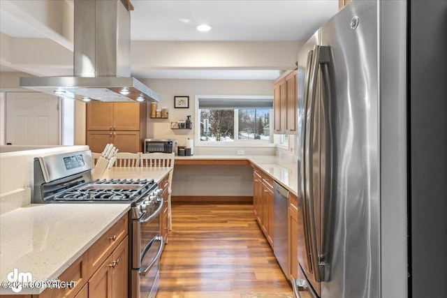 kitchen with stainless steel appliances, island exhaust hood, light wood finished floors, light stone counters, and brown cabinetry