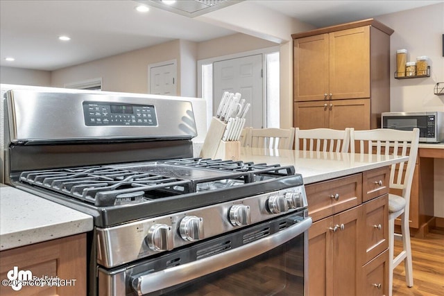 kitchen featuring appliances with stainless steel finishes, light wood-style floors, light stone countertops, brown cabinetry, and recessed lighting