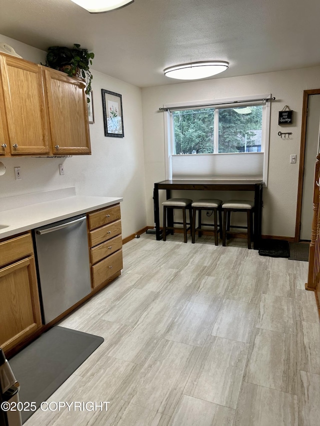 kitchen with stainless steel dishwasher, baseboards, light wood finished floors, light countertops, and brown cabinets