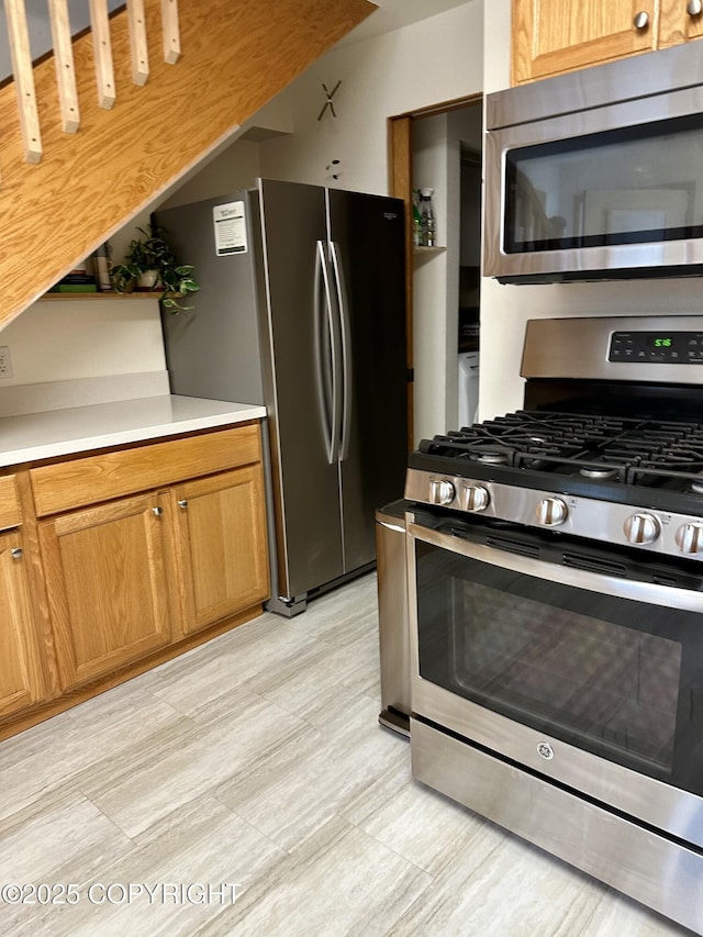 kitchen with appliances with stainless steel finishes, brown cabinetry, light wood-style flooring, and light countertops