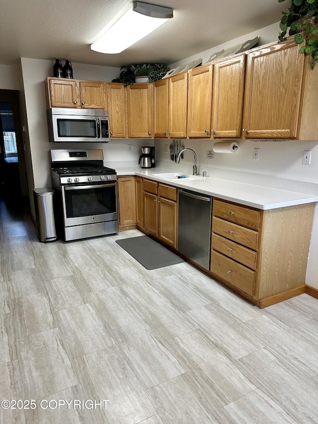 kitchen featuring stainless steel appliances, a sink, light countertops, and light wood finished floors