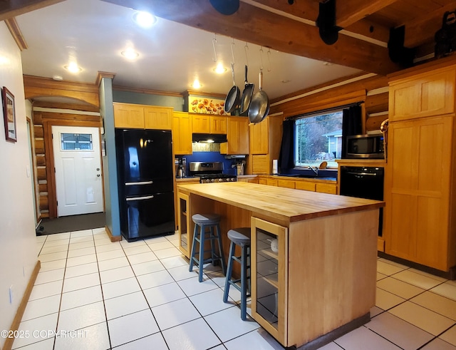 kitchen featuring butcher block counters, appliances with stainless steel finishes, under cabinet range hood, a kitchen bar, and light tile patterned flooring