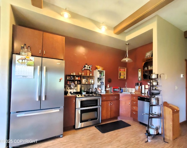 kitchen with stainless steel appliances, light wood finished floors, brown cabinets, a sink, and hanging light fixtures