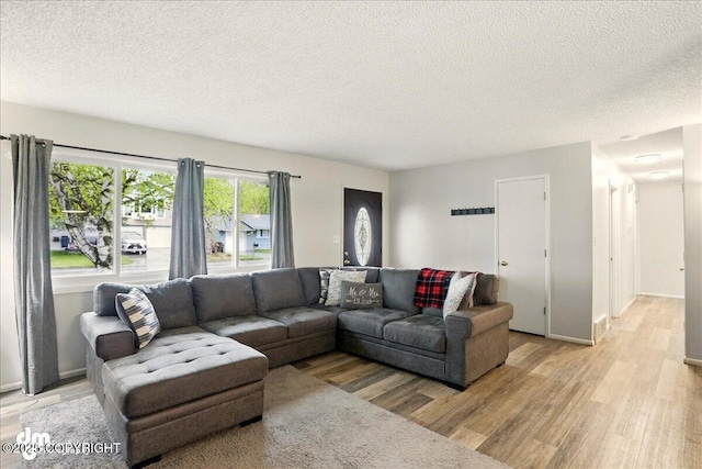 living room featuring a textured ceiling, light wood-style flooring, and baseboards