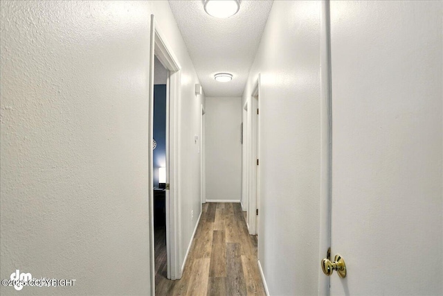 hallway featuring wood finished floors, a textured wall, and baseboards