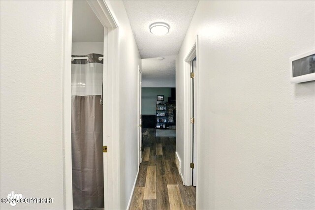 hallway featuring wood finished floors, baseboards, and a textured ceiling