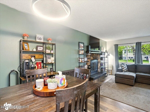 dining space with a textured ceiling, wood finished floors, and a stone fireplace