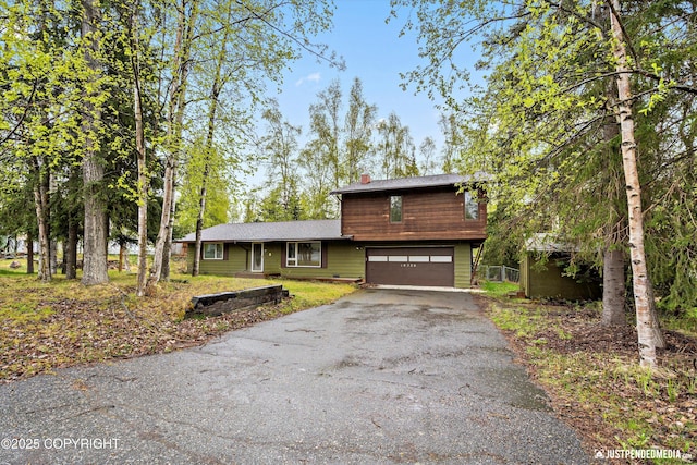 view of front of home featuring asphalt driveway, a garage, and a chimney