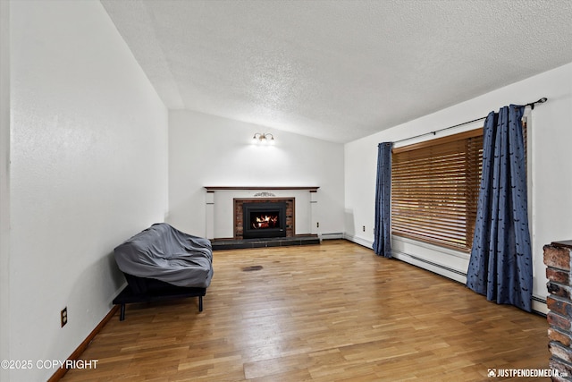 unfurnished living room featuring lofted ceiling, a textured ceiling, light wood-type flooring, a warm lit fireplace, and a baseboard heating unit