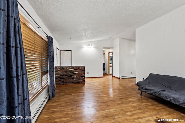 sitting room featuring baseboard heating, a textured ceiling, wood finished floors, lofted ceiling, and baseboards