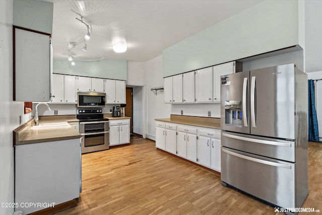 kitchen featuring stainless steel appliances, a sink, white cabinetry, and light wood finished floors