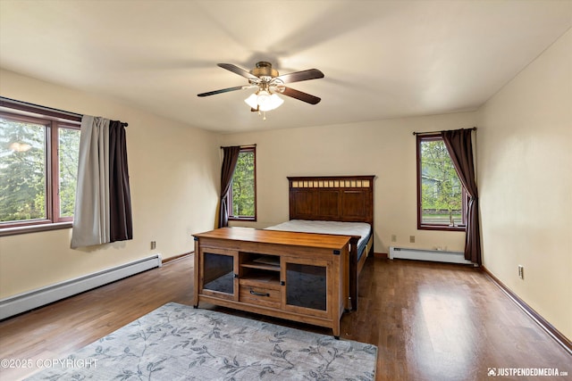 bedroom featuring a baseboard radiator, wood finished floors, and multiple windows