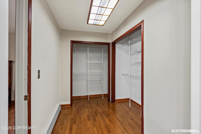 corridor with baseboard heating, wood finished floors, and baseboards