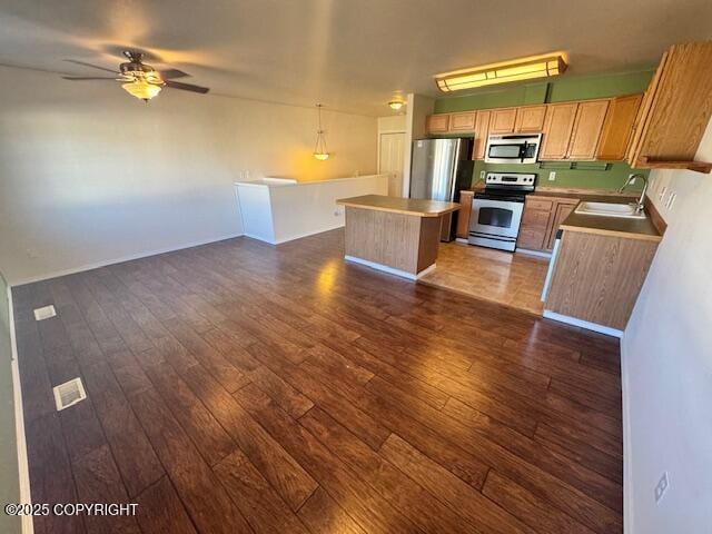 kitchen featuring appliances with stainless steel finishes, a sink, open floor plan, a kitchen island, and dark wood-style flooring