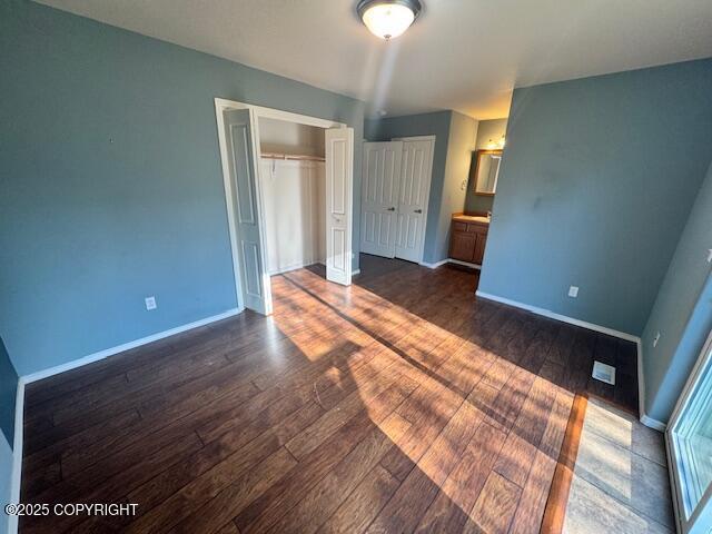 unfurnished bedroom featuring dark wood finished floors, baseboards, and multiple closets