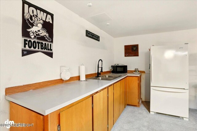 kitchen with freestanding refrigerator, a sink, light colored carpet, black microwave, and brown cabinets