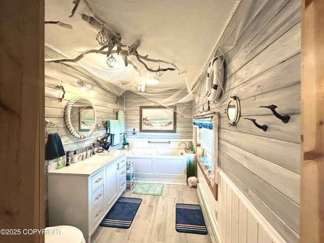 bathroom with a bath, vanity, wooden walls, and wood finished floors