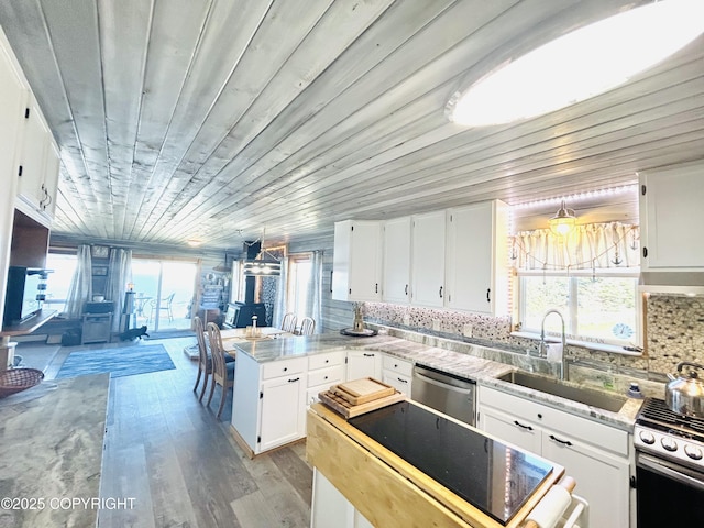kitchen featuring a peninsula, a sink, stainless steel appliances, white cabinetry, and light wood-type flooring