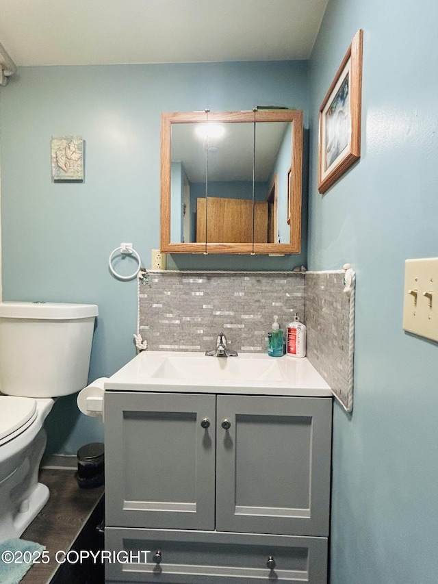 half bathroom featuring decorative backsplash, toilet, vanity, and wood finished floors