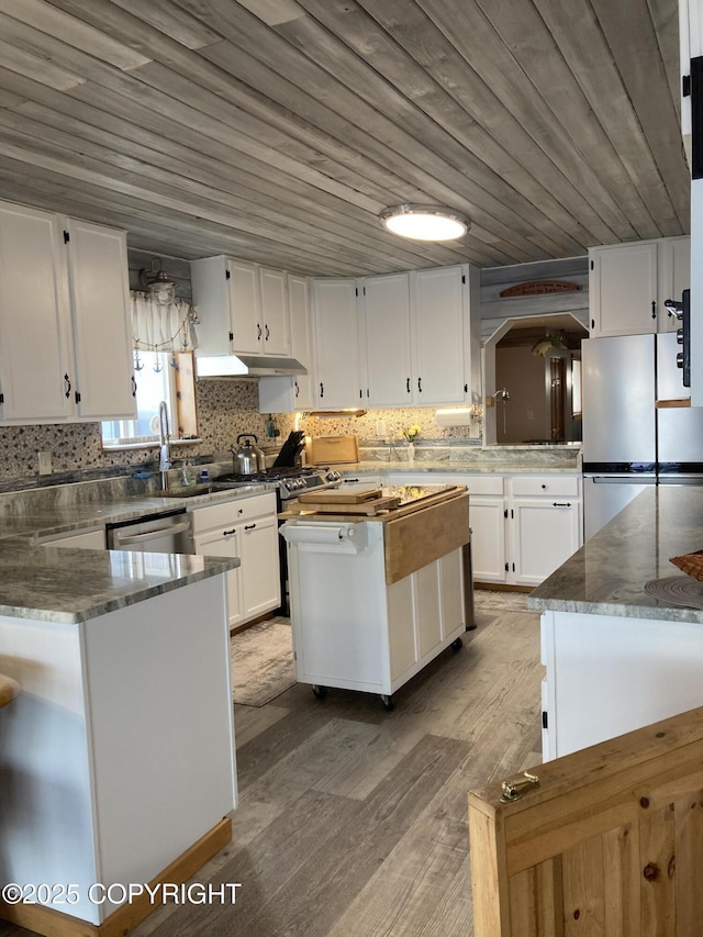 kitchen with appliances with stainless steel finishes, white cabinets, light wood-type flooring, arched walkways, and backsplash