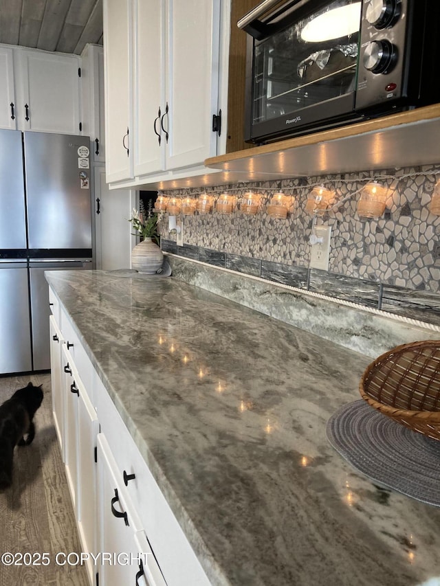 kitchen with freestanding refrigerator, decorative backsplash, black microwave, white cabinetry, and dark stone counters