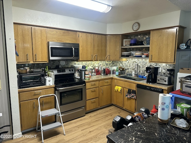 kitchen featuring stainless steel appliances, a sink, tasteful backsplash, light wood-type flooring, and open shelves