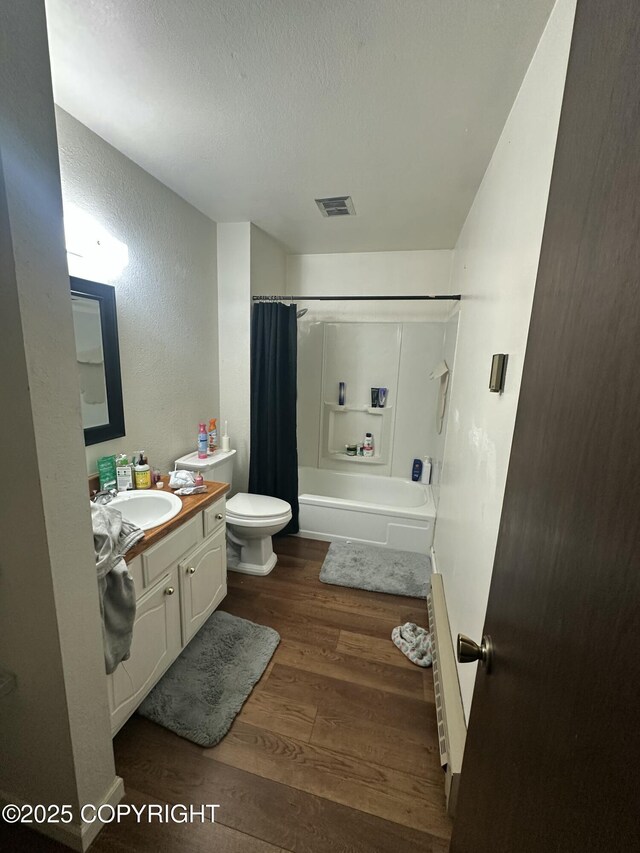 full bathroom featuring wood finished floors, toilet, vanity, a textured ceiling, and shower / bath combo