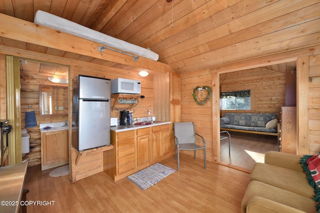 kitchen featuring freestanding refrigerator, white microwave, light wood-style flooring, wooden walls, and light countertops
