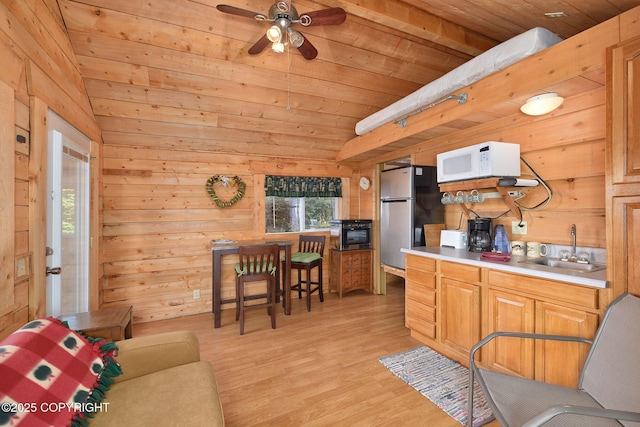kitchen featuring white microwave, a sink, freestanding refrigerator, wood ceiling, and light wood-style flooring