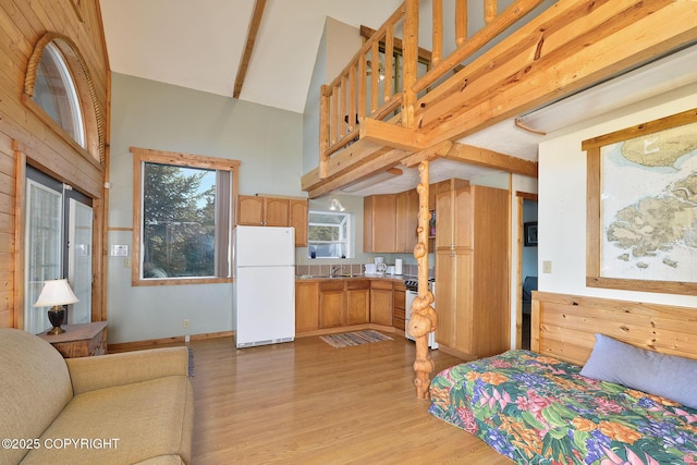 bedroom with freestanding refrigerator, light wood finished floors, a high ceiling, a sink, and baseboards