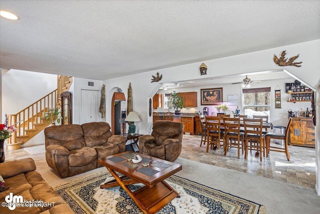 living area featuring arched walkways, stairs, a textured ceiling, and a ceiling fan