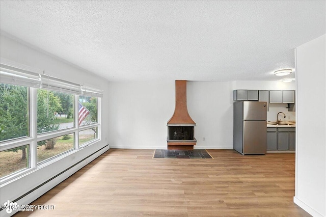 933 W 20th Ave, Anchorage, AK 99503 - unfurnished living room with a baseboard radiator, a wood stove, a textured ceiling, and light wood finished floors